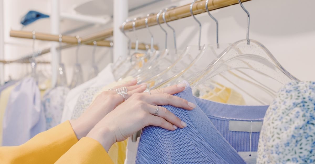 Person browsing colorful sweaters on a clothing rack in a store
