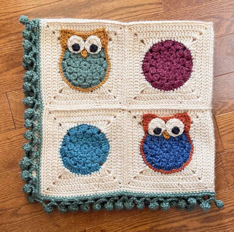 Folded crochet owl afghan showing the finished pom pom border