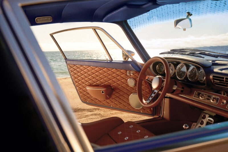 Vintage Porsche 911 with surfboard mounted on roof rack on a beach