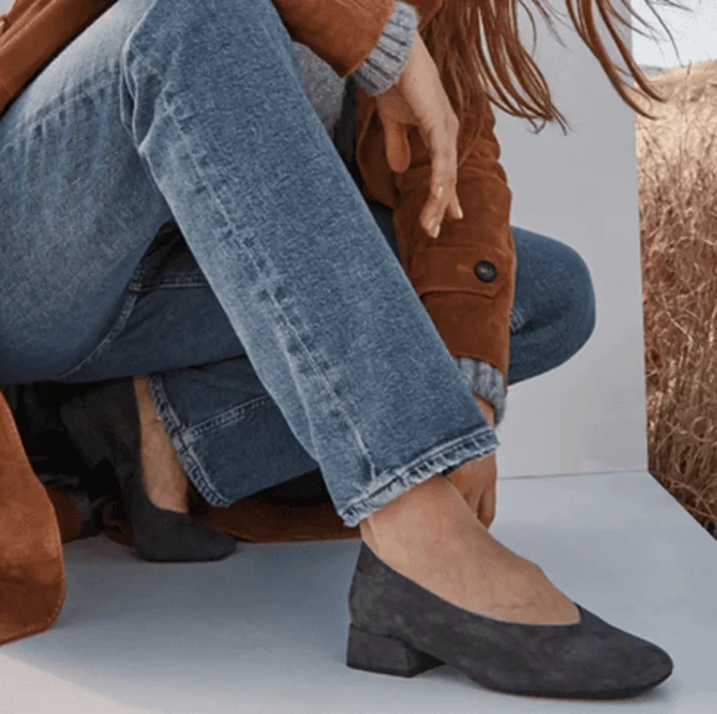 Woman in jeans and brown jacket wearing dark gray low-heeled shoes