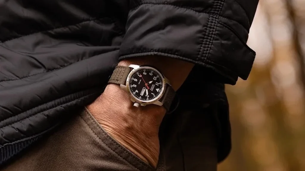 Black dial field watch tucked under a dark jacket cuff
