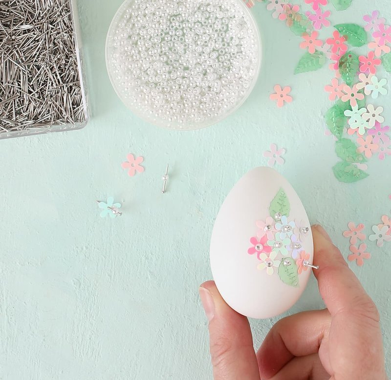 Hand pressing a sequin pin into a foam Easter egg
